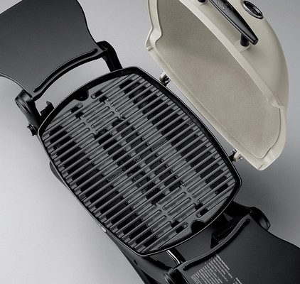 An open electric grill with a ridged surface, showing both the grill plate and the raised lid. The outer casing is black, contrasting with the dark gray cooking surface.