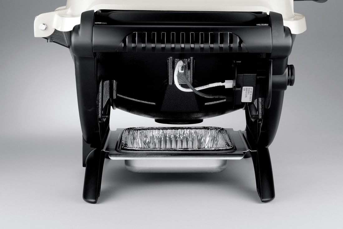 Close-up of the lower portion of an espresso machine with a metal drip tray and a portafilter handle visible. The background is plain and light-colored.