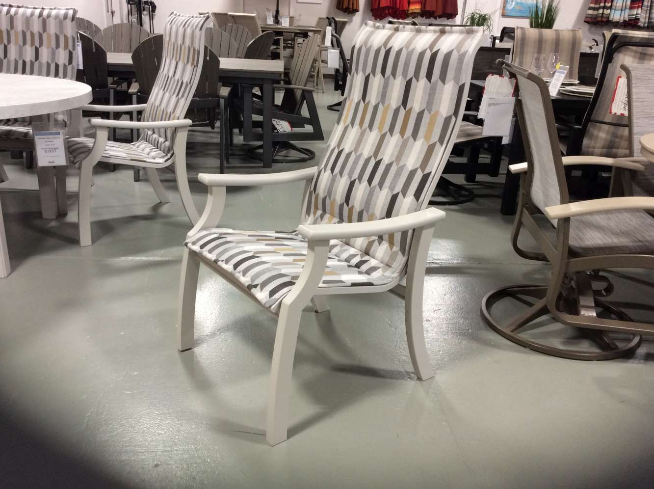 A patterned outdoor chair displayed on a polished concrete floor in a furniture showroom with tables and chairs in the background, near an elegant fire pit.