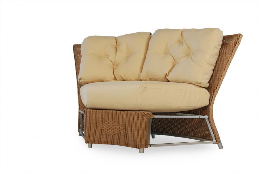 A modern wicker chair featuring plush, beige cushions on a white background. The chair includes a lower shelf for storage near a cozy fireplace.