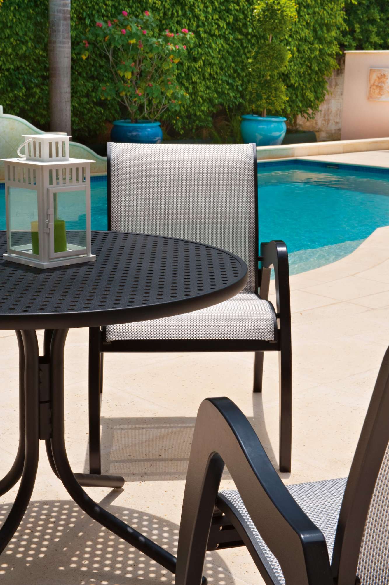 Outdoor furniture set beside a swimming pool, featuring a chair and table with a fire pit on top, surrounded by a neatly landscaped area.
