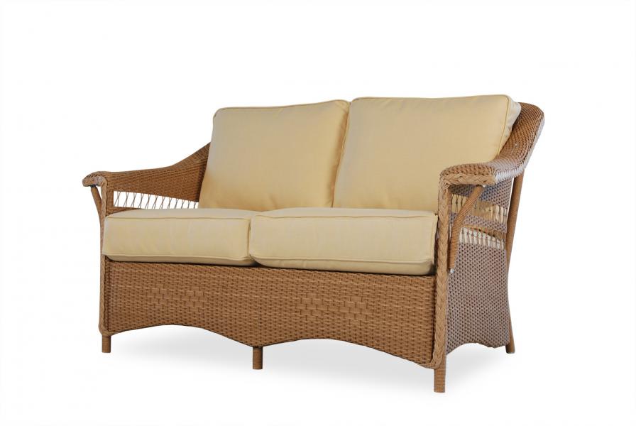 A two-seater wicker sofa with light beige cushions, isolated near a fireplace on a white background.