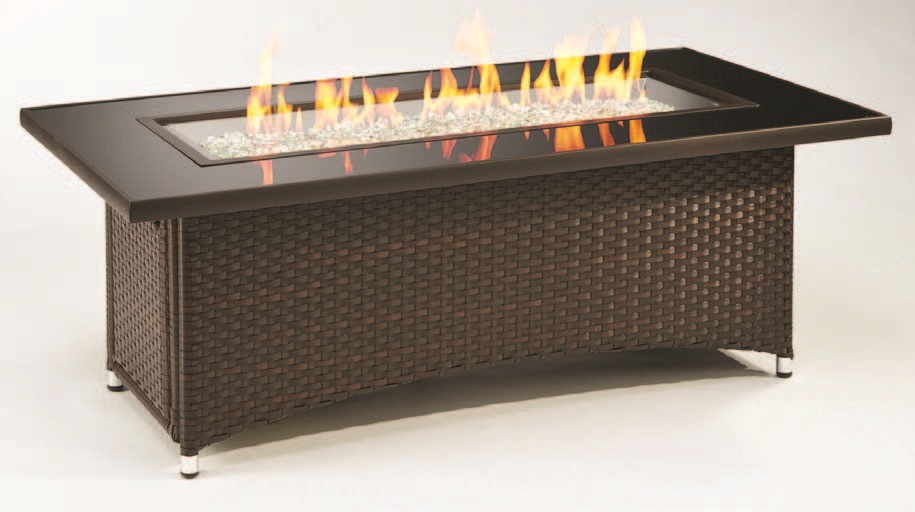 Rectangular fire pit table with a woven base and a glass frame around the flames, showcasing a modern design. Flames are visible over a bed of clear glass rocks.