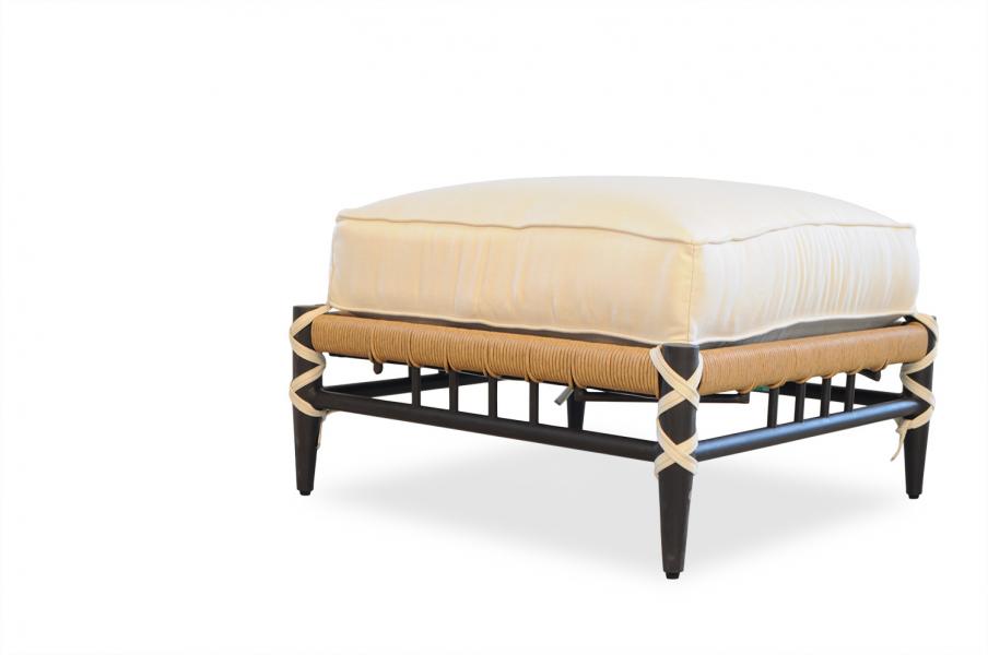 Contemporary ottoman with a thick, cream-colored cushion atop a sleek black metal frame with interwoven tan straps. Insert isolated on a white background.