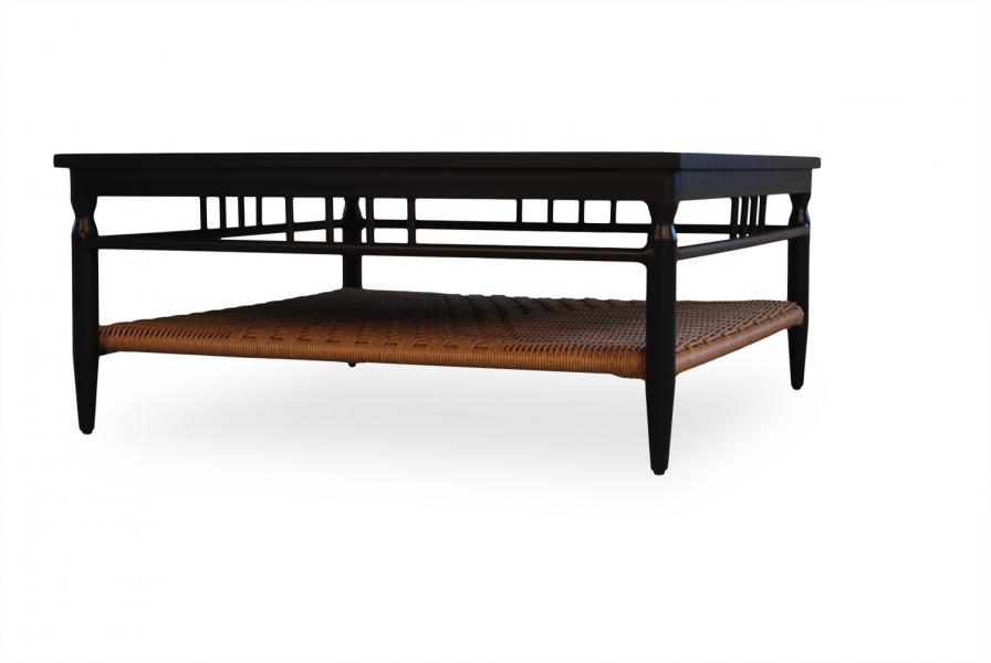 A long, black wooden coffee table with an intricately designed top rail and a woven rattan lower shelf featuring a fireplace insert, isolated on a white background.