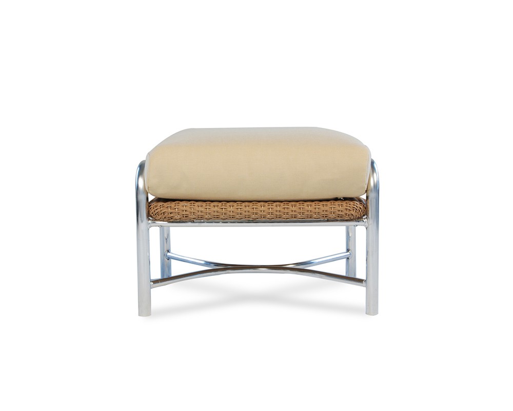 A modern ottoman with a beige cushion on top and a woven rattan shelf below, set within a sleek, silver metal frame with a stove insert, isolated on a white background.