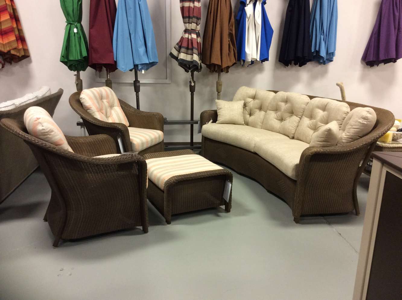 A cozy furniture display with a beige tufted sofa, two matching wicker armchairs with cushions, and a colorful stove inserted in the background.