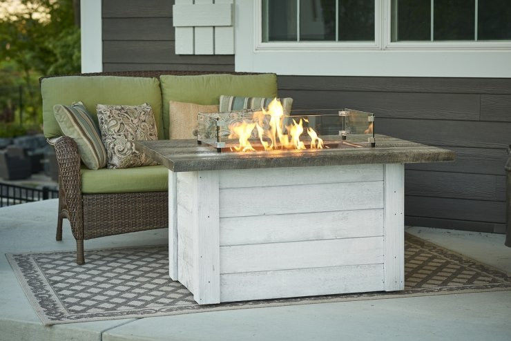 brown and white-colored gas fire pit table in front of a brown wicker sofa with green cushions