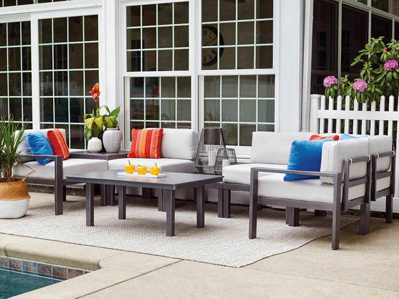 dark gray patio furniture with light gray cushions and a matching table on a tan outdoor rug next to an inground pool and white house