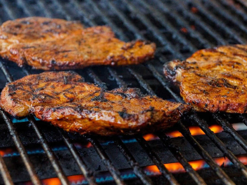 Three steaks with grill marks cooking on a gas grill, with visible flames beneath the grill grate.