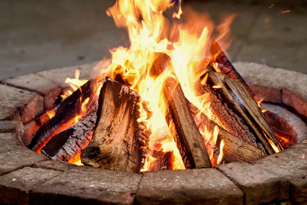 a close-up of a round, wood fire pit made from red bricks with burning logs