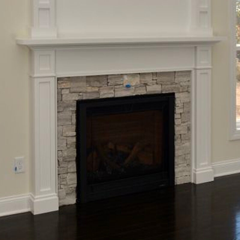 A modern fireplace with a white mantel and gray stone surround, set against a light hardwood floor in a well-lit room.