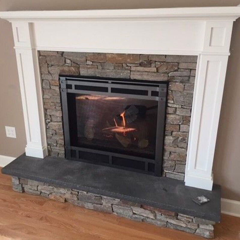 A cozy fireplace with a single burning log inside, framed by a stone surround and a white wooden mantel, set against a light-colored wall in a home.