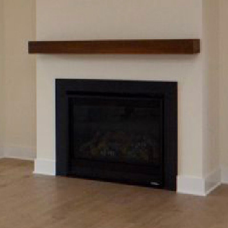 A modern electric fireplace built into a beige wall with a dark frame and a wooden mantel shelf above it. the setting is in a simple, minimalist room.