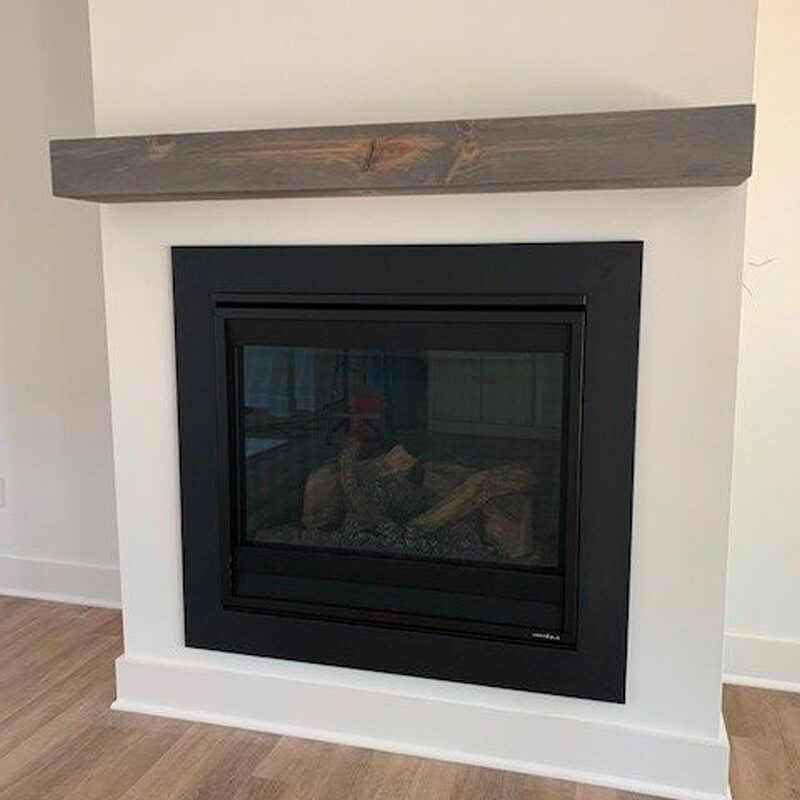 A modern black fireplace with a glass front and decorative logs inside, set within a white wall and topped with a rustic wooden mantel.