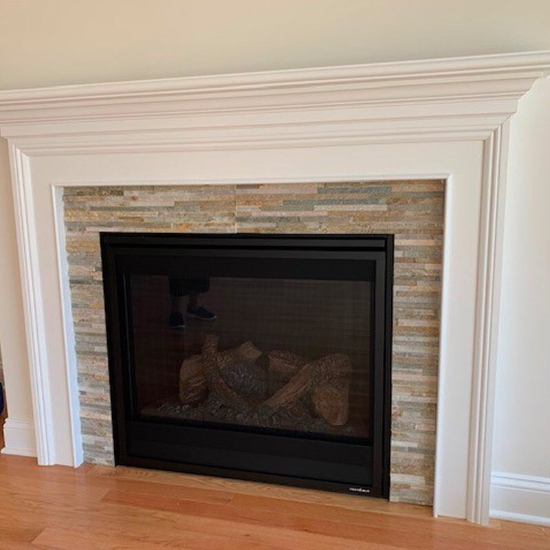 A modern fireplace with a decorative white mantel and a tiled stone surround, featuring a black screen and realistic-looking ceramic logs inside.
