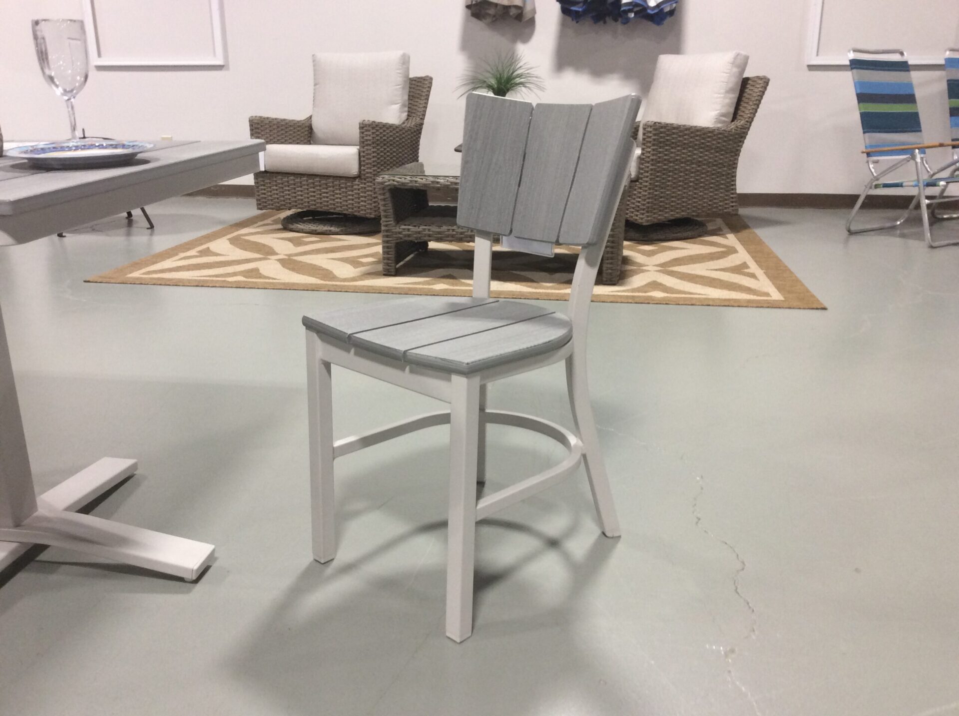 A modern, minimalist indoor setting featuring a gray chair in the foreground and a lounge area with wicker chairs, a couch, and decorative rugs in the background.