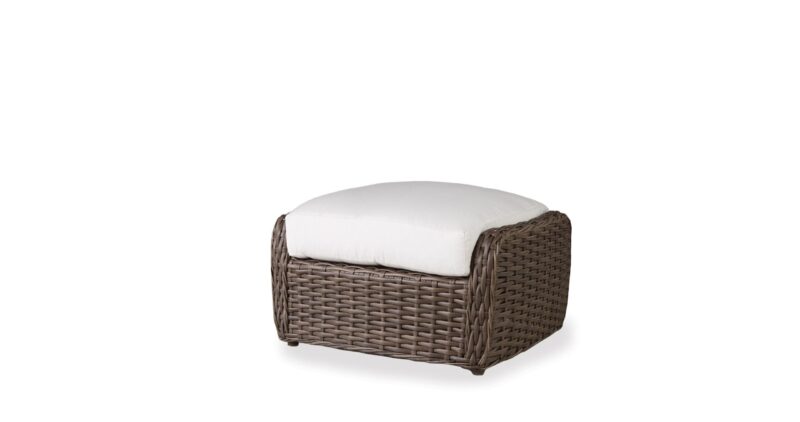A brown wicker ottoman with a white cushion on top, isolated against a white background.