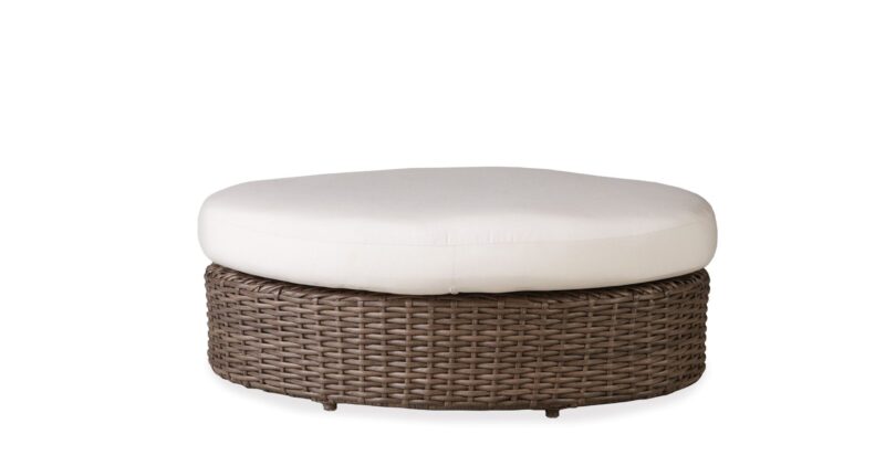 A round, brown wicker ottoman with a thick, white cushion on top, isolated on a white background.