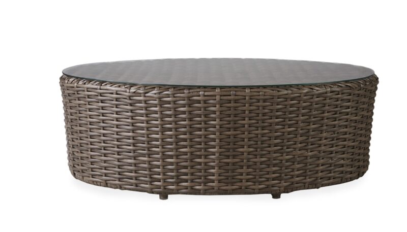 An oval-shaped, wicker coffee table with a flat, smooth glass top, isolated on a white background.