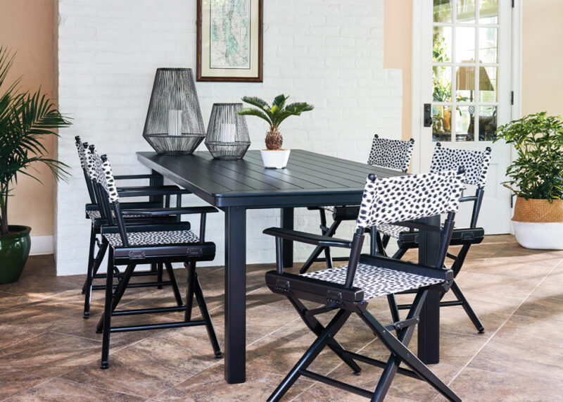 Modern dining area with a black table and chairs featuring white polka dot cushions. the room includes white brick walls, large windows, and decorative plants.