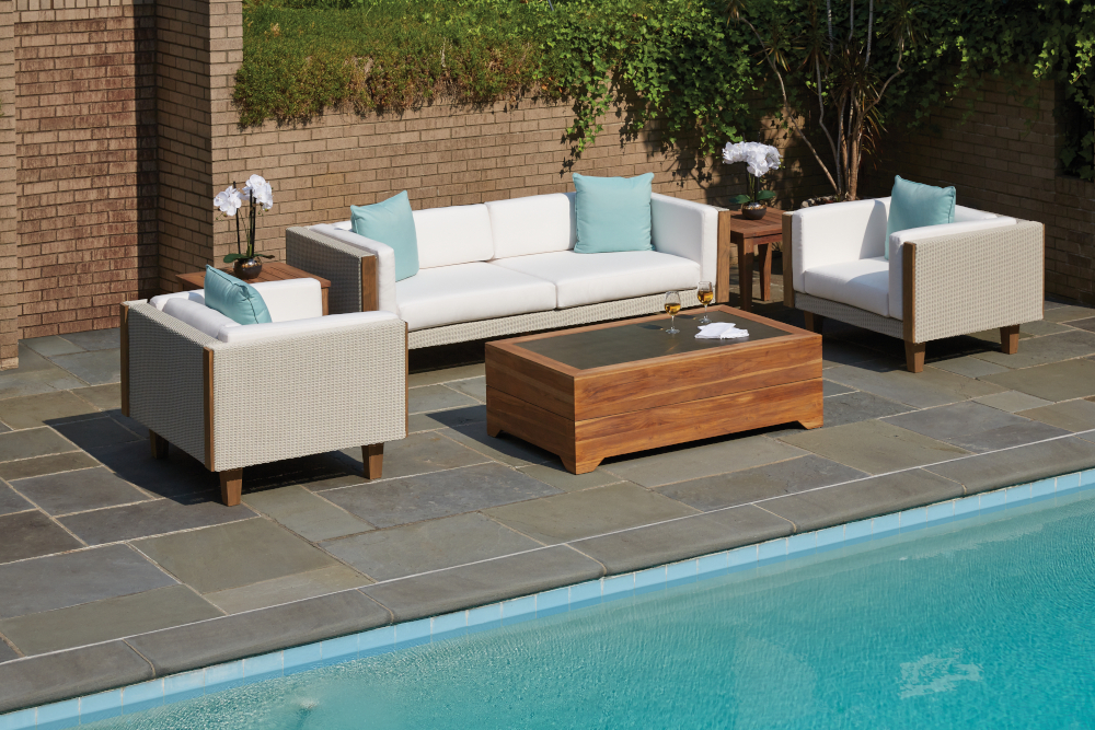 Outdoor patio setup with modern white Catalina sofas, armchairs, and a wooden coffee table next to a swimming pool, surrounded by a garden and brick wall.