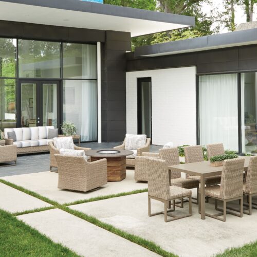 Modern patio area with Milan-inspired wicker furniture and a dining set on a manicured lawn, next to a contemporary house with large glass windows and white walls.