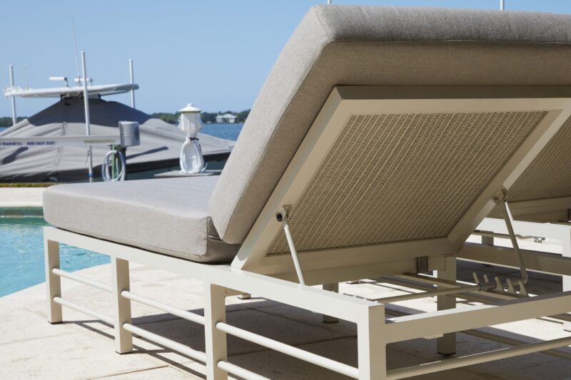 Luxury poolside chaise lounge overlooking a marina with yachts, featuring sleek modern design and plush cushions under clear skies.