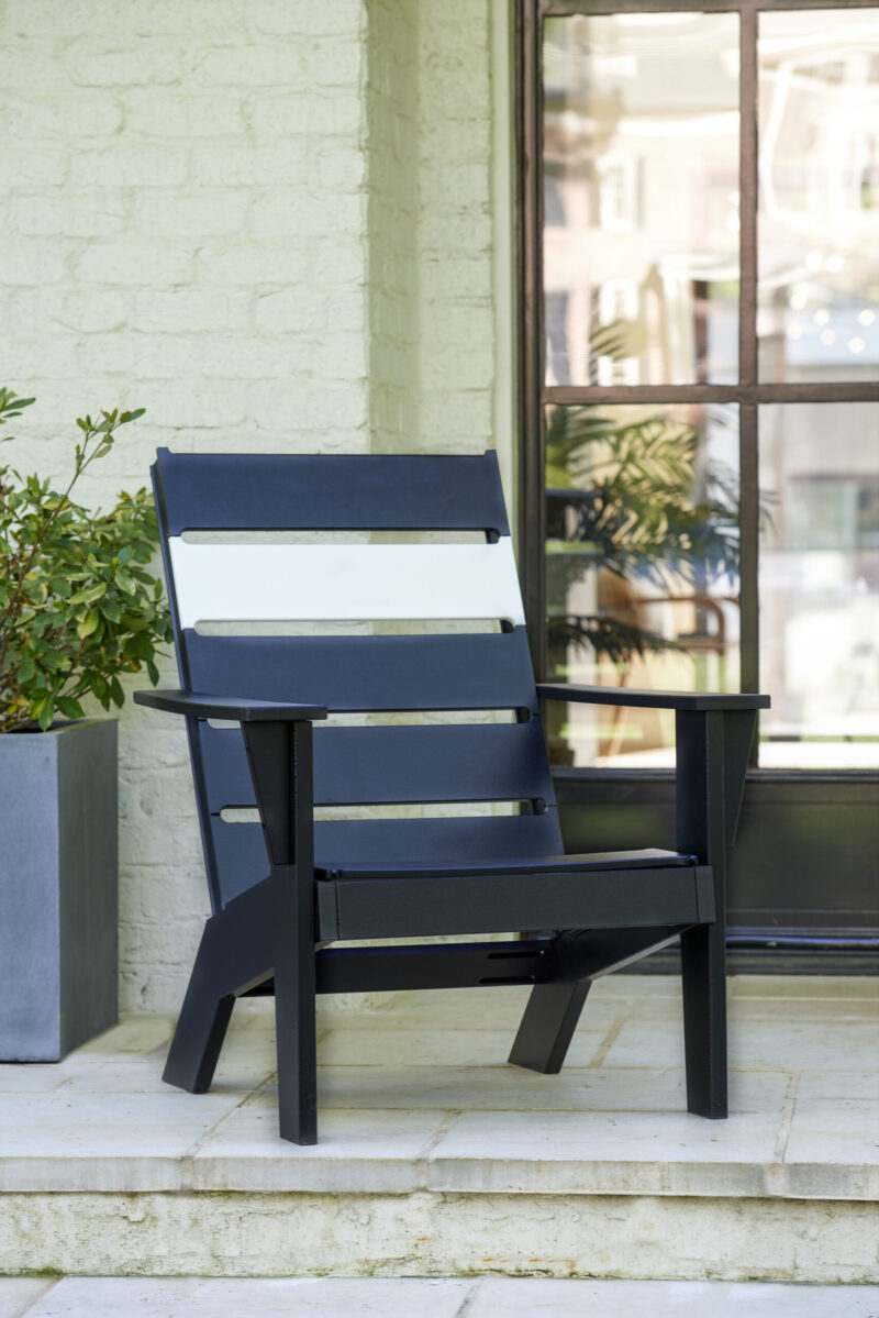 A modern dark blue chair on a porch beside a potted plant, set against a light-painted brick wall and clear glass windows.