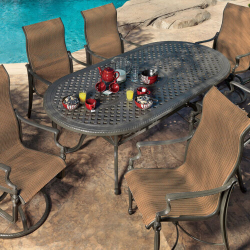 Outdoor dining area with a Gensun Bel Air metal table set for six, featuring wicker chairs near a pool surrounded by rocks and lush greenery.