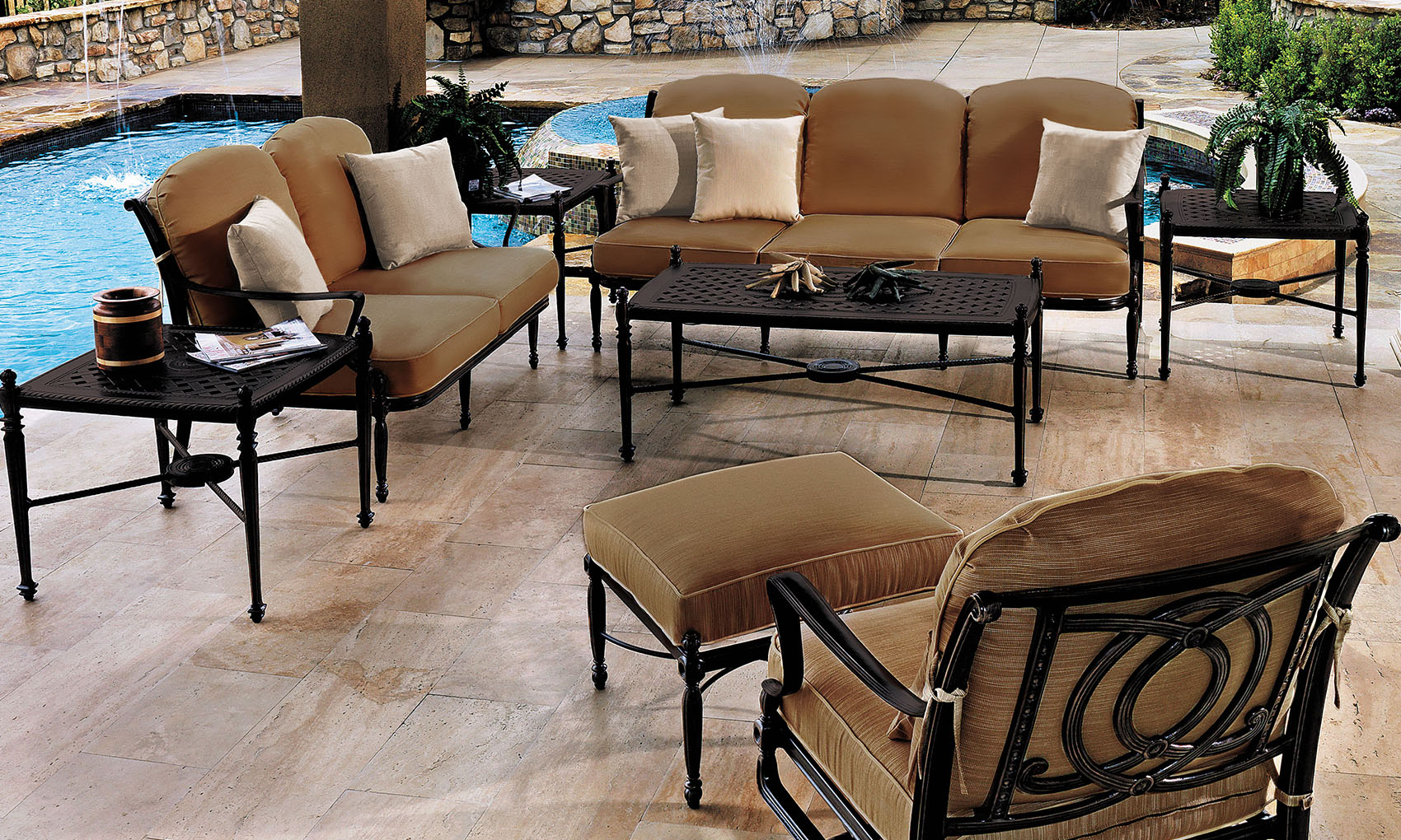 Outdoor patio area featuring a Gensun Bel Air seating arrangement with a sofa, armchairs, and a coffee table, beside a swimming pool surrounded by stone walls and lush greenery.