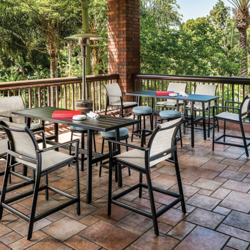 Spacious outdoor terrace with a Gensun Echelon dining area featuring multiple tables and chairs on a terracotta tiled floor, surrounded by lush greenery and equipped with patio heaters.
