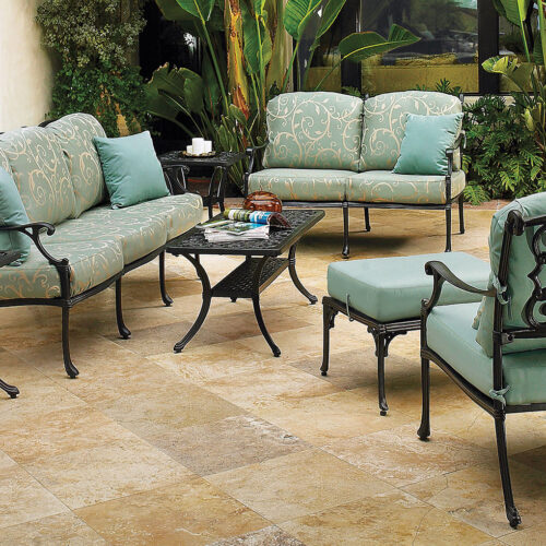 Elegant outdoor patio setting featuring Gensun Michigan metal furniture upholstered in light blue, including a sofa, chairs, and a coffee table, surrounded by lush green plants.