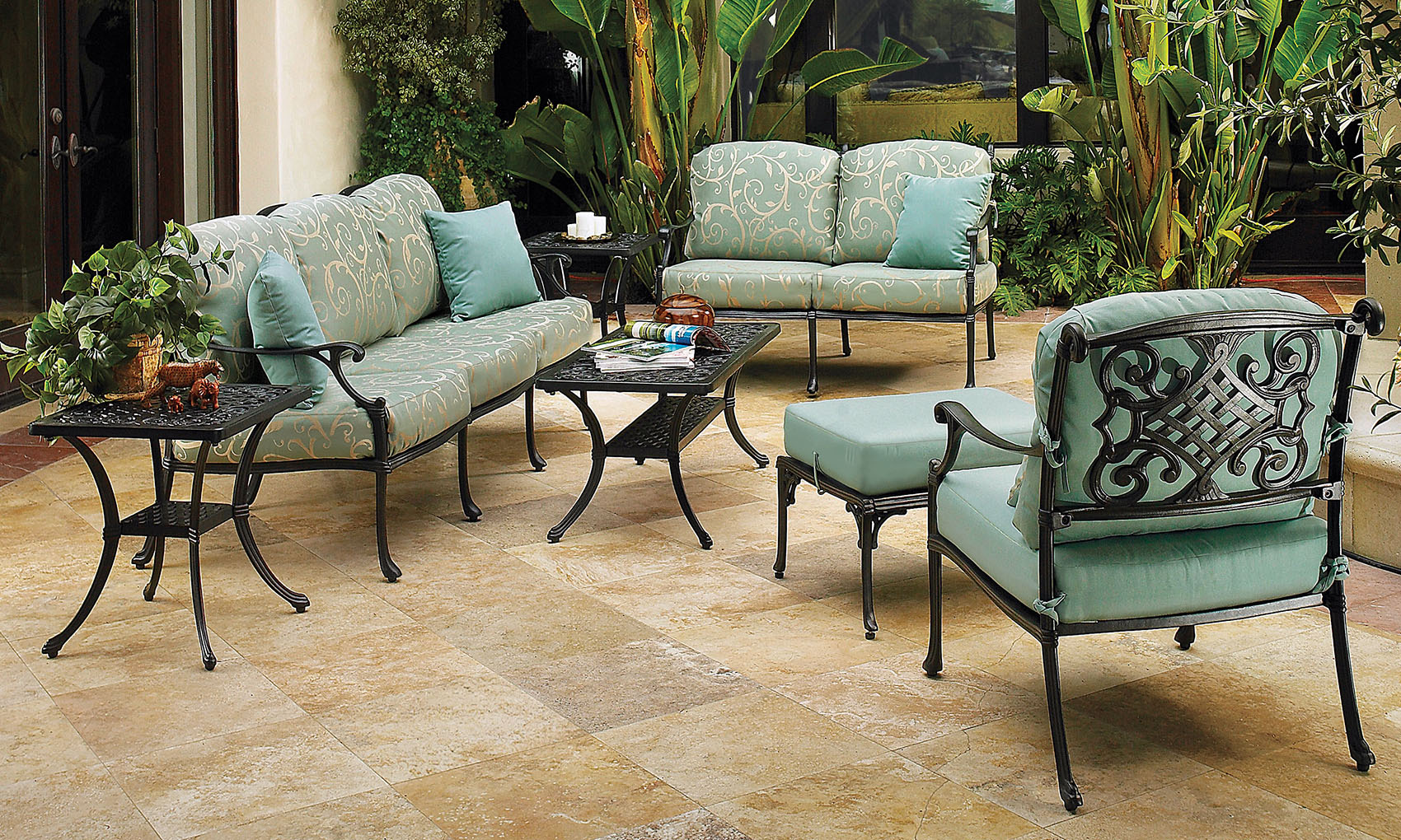 Elegant outdoor patio setting featuring Gensun Michigan metal furniture upholstered in light blue, including a sofa, chairs, and a coffee table, surrounded by lush green plants.
