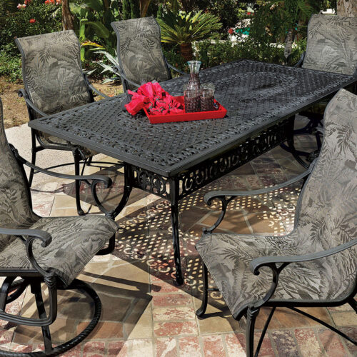 A Gensun Michigan patio dining set featuring a large rectangular metal table and six cushioned chairs in a garden, with a tray on the table under a sunny ambiance.