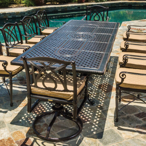 Gensun Grand Terrace metal patio dining set with six chairs on a flagstone surface near a curved swimming pool on a sunny day.
