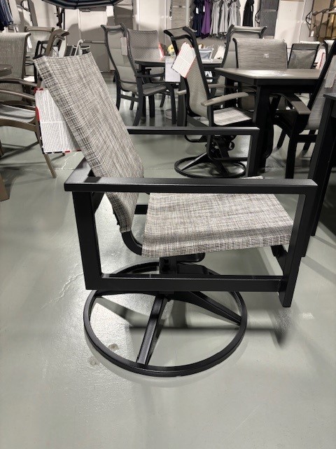 A modern outdoor swivel chair with a black Tribeca frame and white and grey checkered upholstery, displayed in a store with various other furniture in the background.