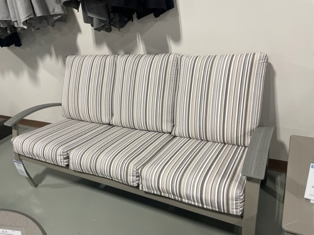 A modern metal-framed sofa with striped cushions in hues of white and gray, situated in a store setting with clothing racks in the background.