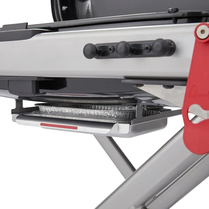 Close-up of a Weber Traveler panini press with a sandwich inside, showcasing the appliance's metallic finish and red handle detail.