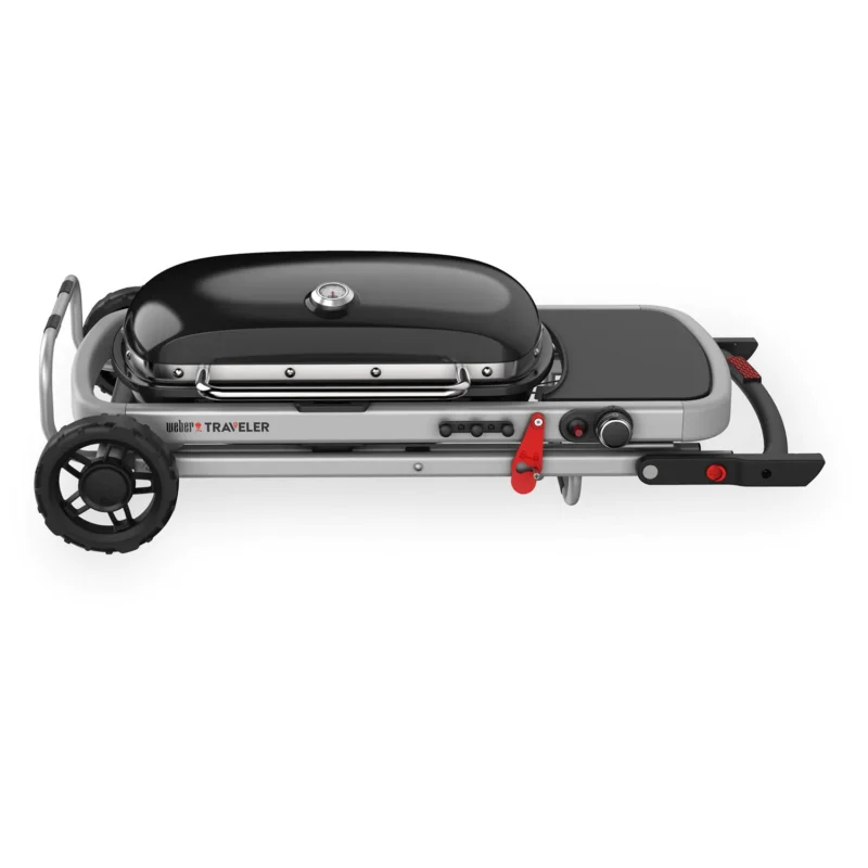 Portable Weber Traveler charcoal grill with a large black lid, silver body, side preparation table, and red accents on handles and knobs, mounted on a wheeled cart for mobility.