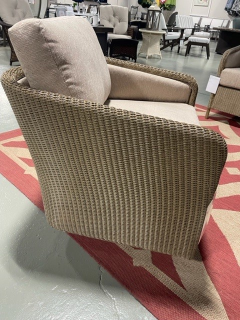 Woven fabric chair with beige upholstery in a furniture showroom, featuring a ribbed texture on the exterior and a smooth seat and back cushion.