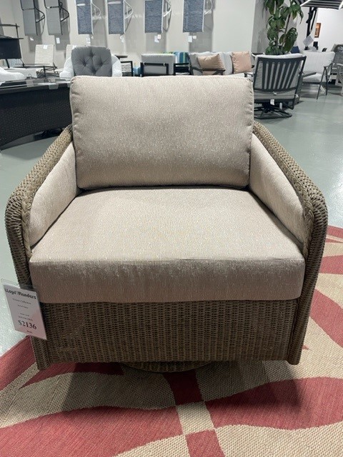 A modern armchair with a beige cushion and woven tan sides, displayed in a furniture store on a red and beige patterned rug. a price tag is visible on the chair.