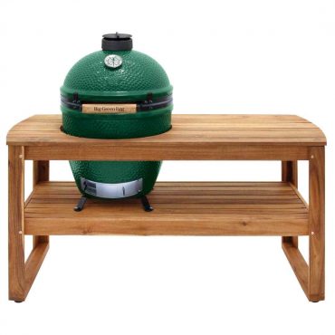 A Big Green Egg ceramic kamado-style grill placed on a wooden table with a lower shelf, isolated against a white background.