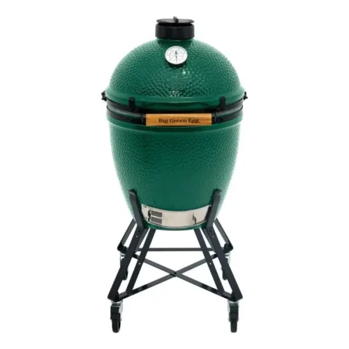 A large green egg grill, an egg-shaped ceramic charcoal grill, is displayed on a metal stand against a white background, featuring a temperature gauge and the brand logo.