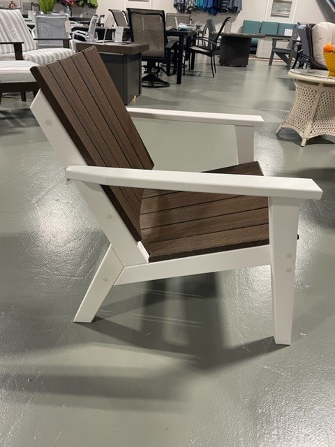 A modern adirondack chair with a white frame and dark brown slats, displayed on a gray showroom floor.