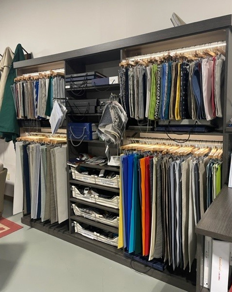 A well-organized fabric sample storage with multiple shelves holding neatly arranged hangers of various fabric swatches in colors and patterns relevant to custom patio sets, and some stacked materials below.