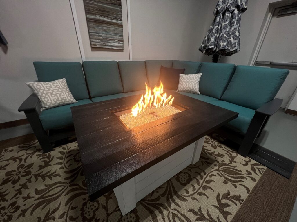 patio table with gas fire pit in the middle surrounded by seating with teal cushions and accent pillows