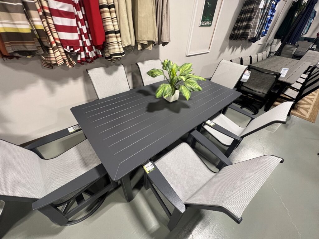 black outdoor patio table with six gray and black chairs and a green plant at the center of the table