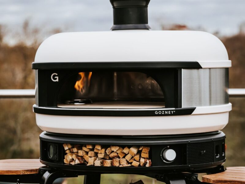 white Gozney Dome oven with a fire inside and chopped wood beneath the oven