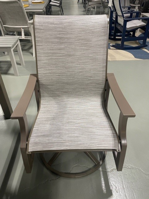 A modern St. Catherine Sling outdoor rocking chair with a gray woven fabric seat and backrest, and dark brown metal frame, displayed in a showroom among other furniture.